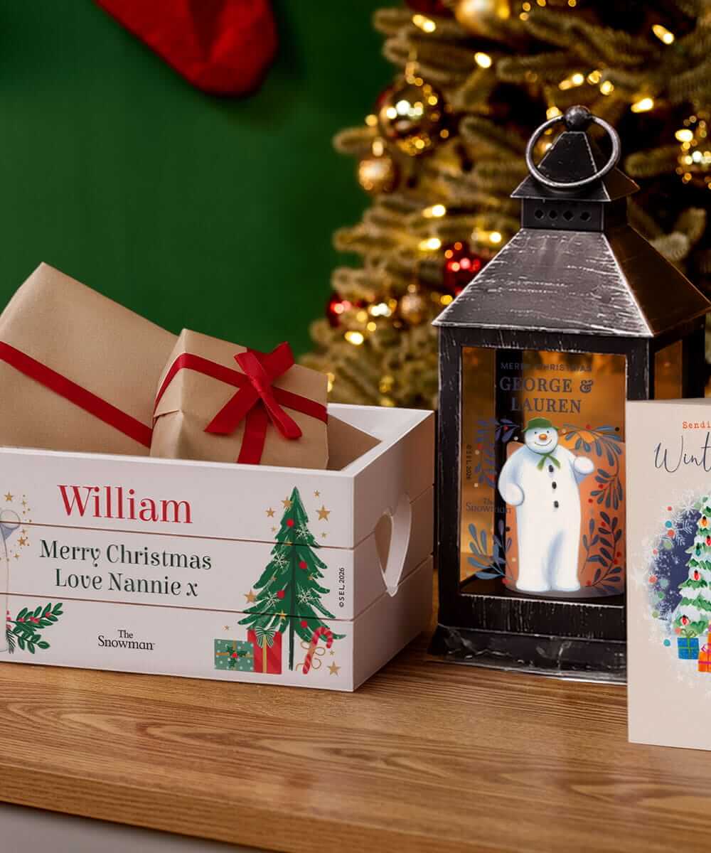 Personalised Christmas Eve box, festive lantern and Christmas card displayed on a wooden table in front of a decorated Christmas tree. Personalised Christmas Eve box, festive lantern and Christmas card displayed on a wooden table in front of a decorated Christmas tree.